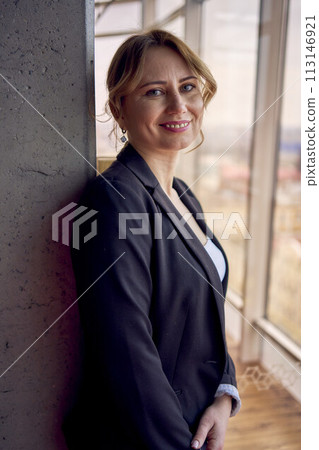 attractive middle age woman in jacket and white t-shirt posing in modern office with panoramic windows 113146921