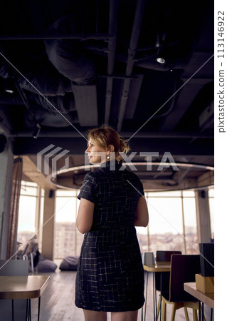 attractive woman in a black mini dress business style walks in a modern coworking space with panoramic windows and a black ceiling 113146922