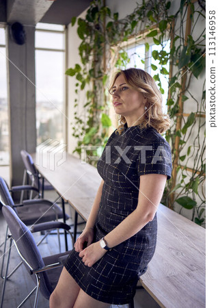 stunning young adult woman in mini dress posing near workspace decorated with green creepers 113146958