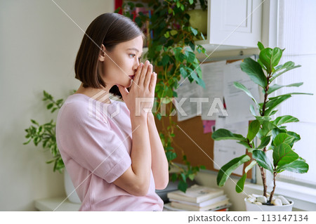 Profile view close-up of young woman's face with hands folded in prayer, dreams 113147134