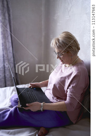 an elderly woman works with laptop at home 113147663
