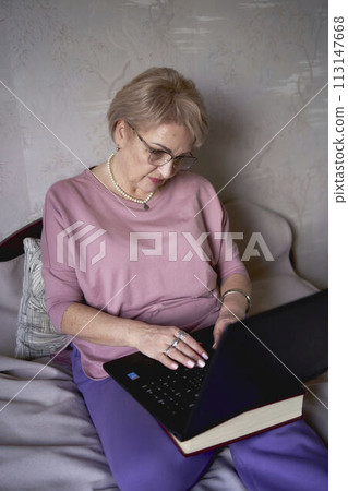 an elderly woman works with laptop at home 113147668