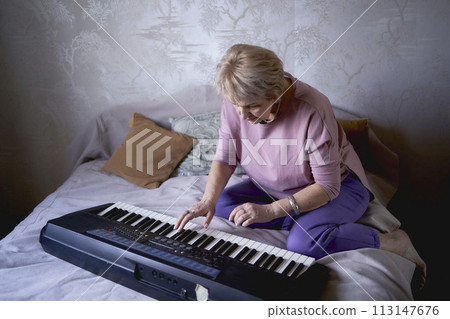 A 60-year-old mother and a 40-year-old daughter play the keyboard together on the bed at home A 60-year-old mother and a 40-year-old daughter play the keyboard together on the bed at home 113147676
