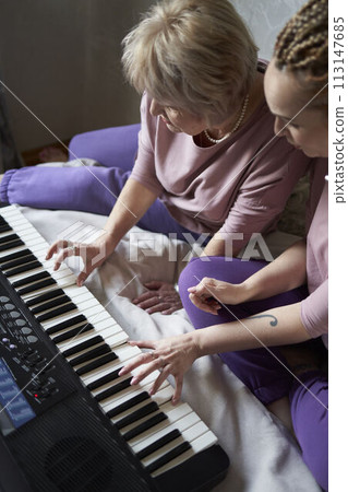 A 60-year-old mother and a 40-year-old daughter play the keyboard together on the bed at home A 60-year-old mother and a 40-year-old daughter play the keyboard together on the bed at home 113147685