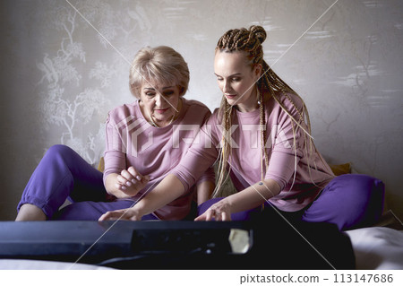 A 60-year-old mother and a 40-year-old daughter play the keyboard together on the bed at home A 60-year-old mother and a 40-year-old daughter play the keyboard together on the bed at home 113147686