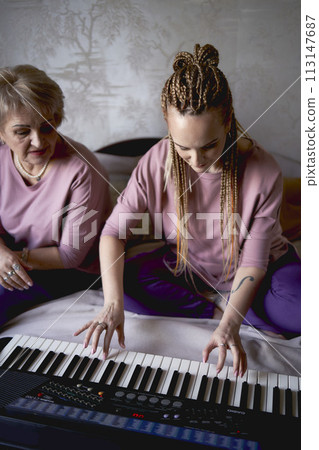 A 60-year-old mother and a 40-year-old daughter play the keyboard together on the bed at home A 60-year-old mother and a 40-year-old daughter play the keyboard together on the bed at home 113147687