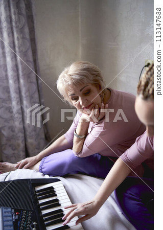 A 60-year-old mother and a 40-year-old daughter play the keyboard together on the bed at home A 60-year-old mother and a 40-year-old daughter play the keyboard together on the bed at home 113147688