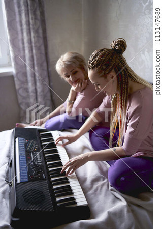 A 60-year-old mother and a 40-year-old daughter play the keyboard together on the bed at home A 60-year-old mother and a 40-year-old daughter play the keyboard together on the bed at home 113147689