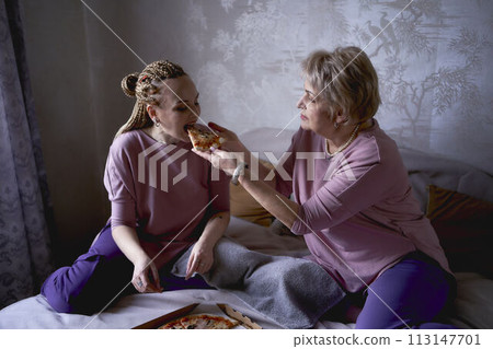 old mother and middle-aged daughter eating pizza and watching a movie at home old mother and middle-aged daughter eating pizza and watching a movie at home 113147701