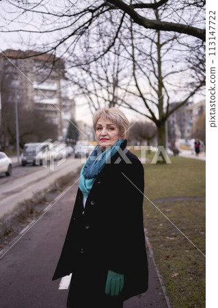 portrait of a stylish old woman in a black coat with green accessories on a spring street 113147722