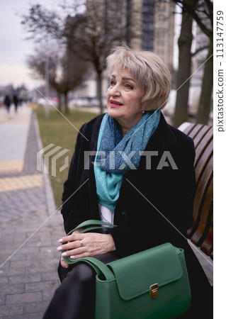 portrait of a stylish old woman in a black coat with green accessories on a spring street 113147759