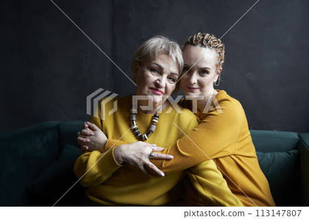stylish old mother and middle-aged daughter in yellow sweaters hug and comfort each other in a cafe 113147807
