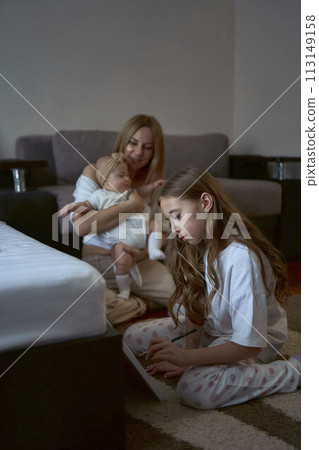 girl paint on the floor while her mother plays with baby sister 113149158
