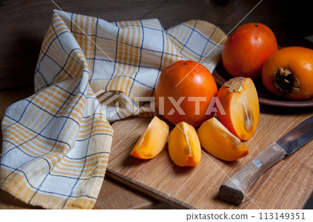Whole ripe persimmon and sliced fruit on a wooden background.. 113149351