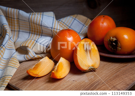 Whole ripe persimmon and sliced fruit on a wooden background.. 113149353