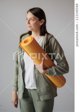 young woman practicing yoga or stretching. girl in training stands with yellow yoga mat in hands 113149389