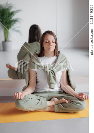 young woman practicing yoga in gym meditates, eyes closed in lotus position. Yoga balance relaxation 113149395