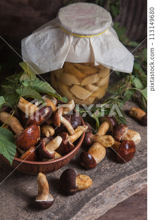 Pile of Imleria Badia or Boletus badius mushrooms commonly known as the bay bolete with canned mushroom in glass jar on vintage wooden background.. Pile of Imleria Badia or Boletus badius mushrooms commonly known as the bay bolete with canned mushroom in glass jar on vintage wooden background.. 113149680