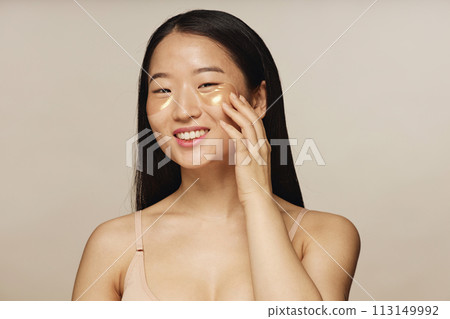 Medium closeup studio shot of young Asian woman posing for camera with collagen patches under eyes 113149992