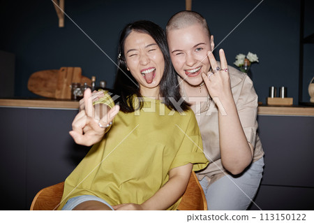 Two ethnically diverse girl friends wearing casual clothes having fun posing for camera in kitchen, flash photo Two ethnically diverse girl friends wearing casual clothes having fun posing for camera in kitchen, flash photo 113150122