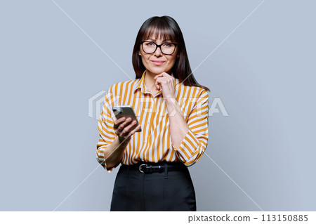 Middle aged smiling woman with smartphone on grey studio background 113150885