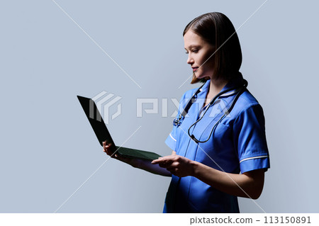 Female nurse using laptop, profile view on gray studio background 113150891