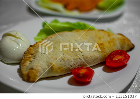 Calzone Stuffed Pizza. Homemade Italian Meat and Cheese Calzones with Sauce. Mozzarella cheese and tomatoes on a white plate Calzone Stuffed Pizza. Homemade Italian Meat and Cheese Calzones with Sauce. Mozzarella cheese and tomatoes on a white plate 113151037