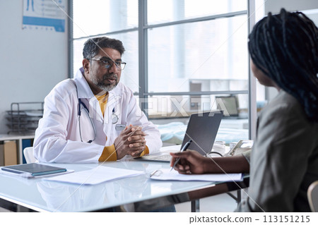 Portrait of senior doctor consulting Black woman sitting across table at workplace in medical clinic copy space 113151215