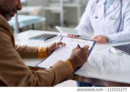Over shoulder view of mature Middle Eastern man writing on clipboard in clinic and filling in medical information copy space Over shoulder view of mature Middle Eastern man writing on clipboard in clinic and filling in medical information copy space 113151277