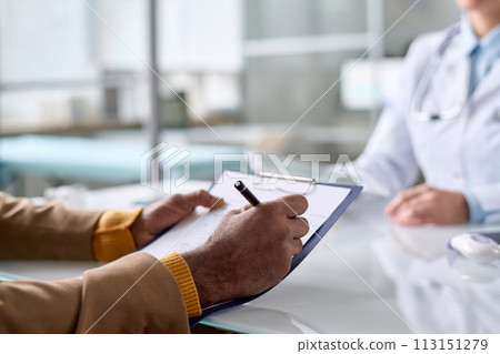 Close up of unrecognizable man holding clipboard in clinic and writing medical information copy space 113151279