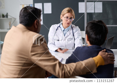 Portrait of mature woman doctor consulting Middle Eastern father and son in sitting across table in pediatric clinic Portrait of mature woman doctor consulting Middle Eastern father and son in sitting across table in pediatric clinic 113151287