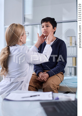 Vertical portrait of pediatrician examining neck and throat of young boy during health check up in clinic Vertical portrait of pediatrician examining neck and throat of young boy during health check up in clinic 113151319