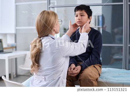 Back view of female doctor examining neck and throat of young boy during health check up in pediatric clinic 113151321