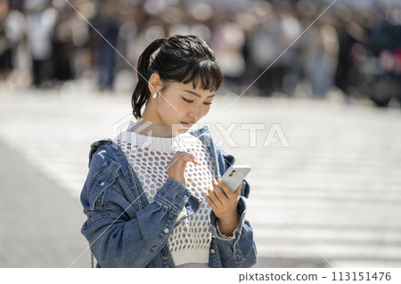 一名十幾歲的女性在城裡操作智慧型手機 一名十幾歲的女性在城裡操作智慧型手機 113151476