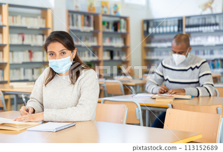 Woman wearing mask studying in public library Woman wearing mask studying in public library 113152689