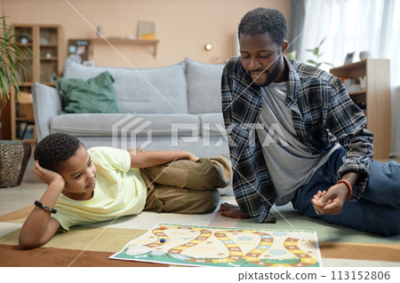 Full length portrait of Black father and son playing board game together sitting on floor at home enjoying family time Full length portrait of Black father and son playing board game together sitting on floor at home enjoying family time 113152806