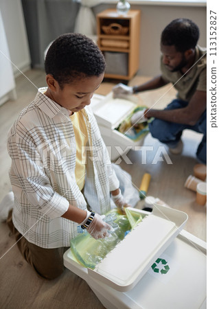 High angle view at young African American boy sorting waste at home and putting plastic bottle into bin for recycling 113152827