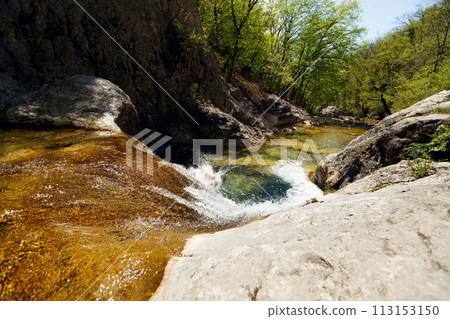 Young Man Jumping From Cliff Into Water of Mountain River 113153150
