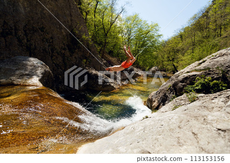 Young Man Jumping From Cliff Into Water of Mountain River Young Man Jumping From Cliff Into Water of Mountain River 113153156