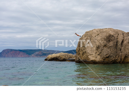 Brave Man Jumps From High Cliff Rock Into Water of Sea 113153235