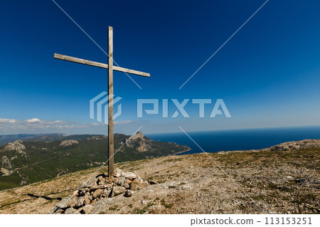 Christian wooden cross on mountain top, rocky summit, beautiful inspirational landscape with ocean, clouds and blue sky, looking at scenic blue sea and white clouds Christian wooden cross on mountain top, rocky summit, beautiful inspirational landscape with ocean, clouds and blue sky, looking at scenic blue sea and white clouds 113153251