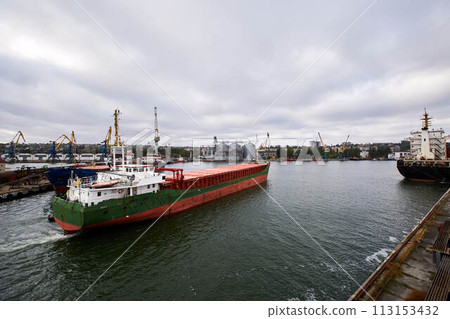 Large bulk ship entering the harbour of commercial dock at seaport to load at grain terminal elevators with wheat and other crops. Large bulk ship entering the harbour of commercial dock at seaport to load at grain terminal elevators with wheat and other crops. 113153432
