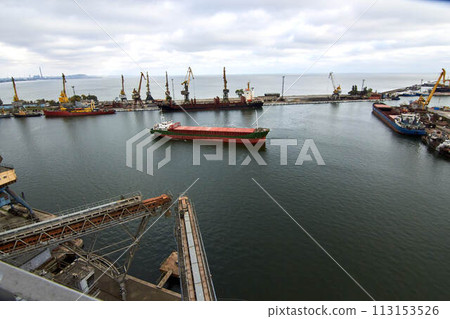 Large bulk ship entering the harbour of commercial dock at seaport to load at grain terminal elevators with wheat and other crops. Large bulk ship entering the harbour of commercial dock at seaport to load at grain terminal elevators with wheat and other crops. 113153526