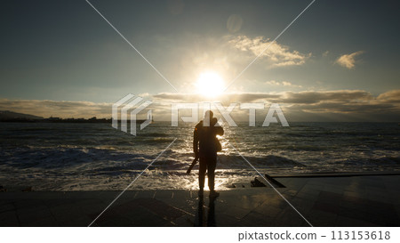 Silhouette of a man photographing the wave. Tourist photographer shoots stormy sea on wet embankment 113153618