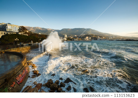 Storm at the sea and embankment street in the morning on. Big waves and tides wash against with lots of foam and splashes on sunrise. 113153623