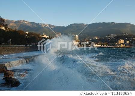 Storm at the sea and embankment street in the morning on. Big waves and tides wash against with lots of foam and splashes on sunrise. 113153624
