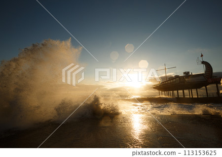 Storm at the sea and embankment street in the morning on. Big waves and tides wash against with lots of foam and splashes on sunrise. Storm at the sea and embankment street in the morning on. Big waves and tides wash against with lots of foam and splashes on sunrise. 113153625