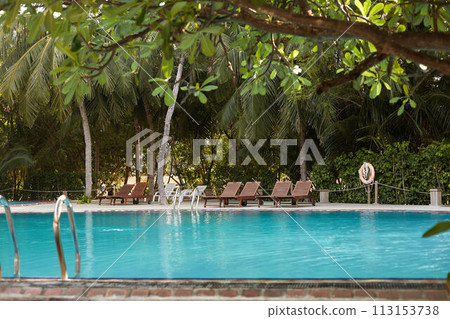 Swimming pool side of luxury hotel ith deck chairs, palm trees and blue ocean. Maldives 113153738