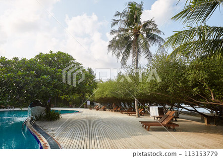Swimming pool side of luxury hotel ith deck chairs, palm trees and blue ocean. Maldives 113153779