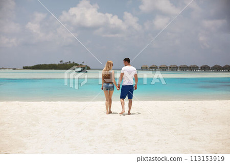Back view of couple holding hands and walking to the blue ocean lagoon on Maldives at luxury spa resort. Travel and honeymoon concept. 113153919